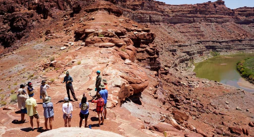 A group of people stand in a circle on red canyon walls above a river